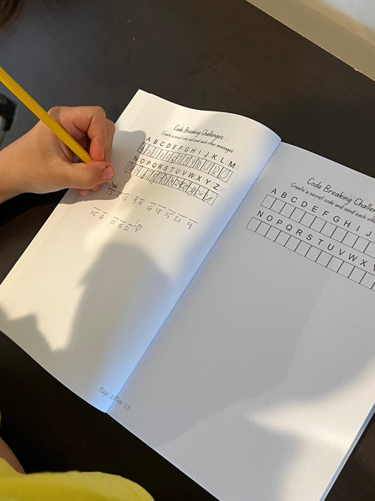 Person holding a pencil over an open book with code-breaking challenges.